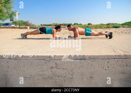 Fit young man and woman exercising on the beach. Smiling caucasian couple doing plank, core workout. Stock Photo