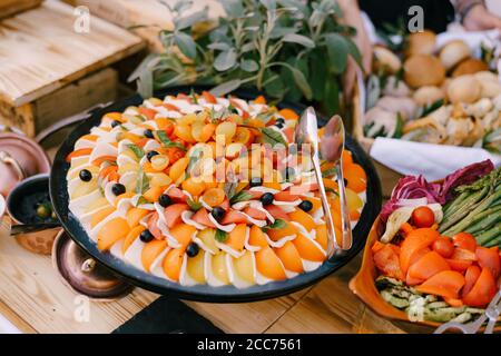 Close-up of caprese vegetable appetizer on a platter on a table with vegetable slices and flowers in pots. Stock Photo