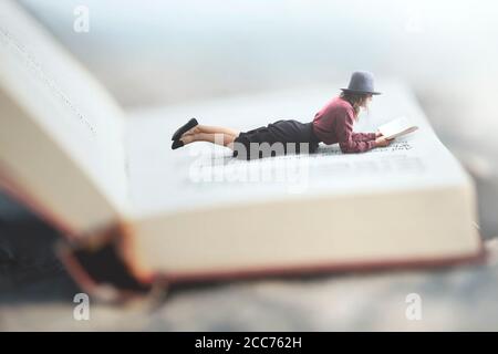 surreal situation of a woman reading her book lying on a giant book Stock Photo