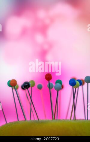 Pin cushion with multi coloured pins and a pink background Stock Photo