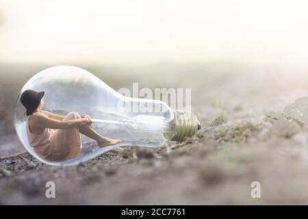 surreal moment of a small woman resting inside a light bulb Stock Photo