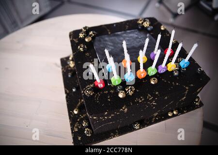 happy birthday lettering on candles on cake, square cake in black cream, golden spots on sweets Stock Photo