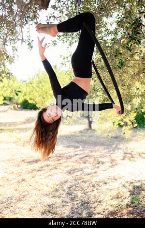 Acrobat making a pose on aerial hoop among olive trees in summer. Stock Photo