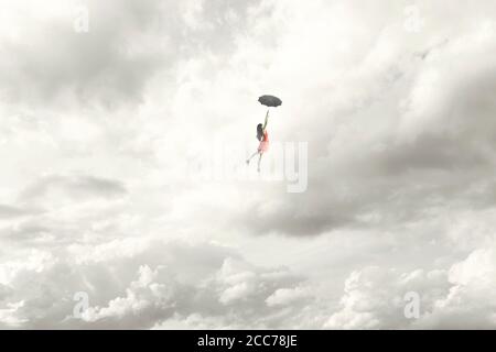 Surreal moment of an elegant woman flying in the middle of the clouds hanging on her umbrella Stock Photo