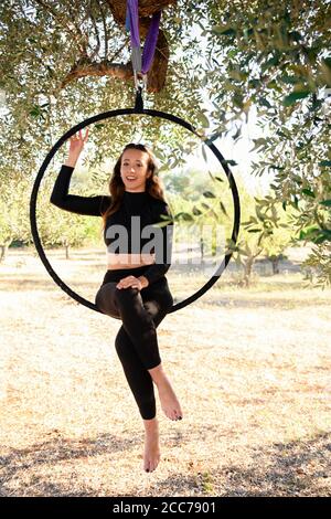 Acrobat making a pose on aerial hoop among olive trees in summer. Stock Photo