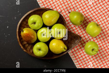 Flat lay photo - vintage wood carved bowl with apples and pears, red chequered tablecloth on black board Stock Photo