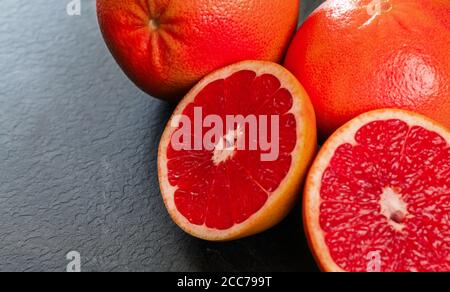 Pink grapefruits halves, whole citrus in background, on black slate like board Stock Photo