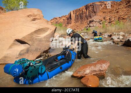 Mylène Jacquemart and Robert Hahn walk their packrafts over a shallow section on the Escalante River near Scorpion Gulch, Utah. Stock Photo