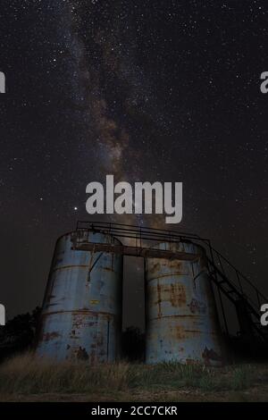 Galactic core milky way rises behind two unused water storage tanks in arid plains of central west texas. foreground composte with stacked star. Stock Photo