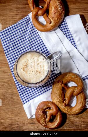 Glass of lager beer with traditional salted pretzels on white and blue napkin over wooden background. Flat lay, space. Oktoberfest theme Stock Photo