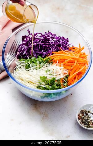 Lady pouring the dressing on the  vegan coleslaw in the mixing bowl Stock Photo