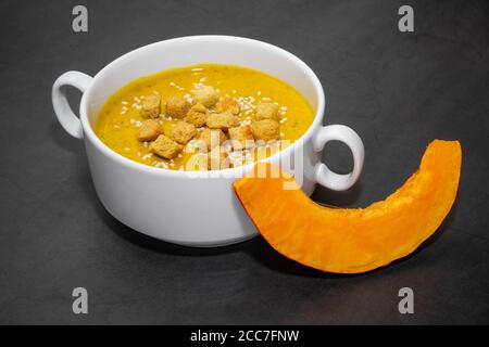 Pumpkin cream soup with crackers on a dark background. Pumpkin cream soup with crackers and sesame seeds in a white bouillon on a dark background Stock Photo