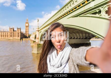London travel selfie tourist woman making silly faces. Funny Asian girl sticking out tongue doing cheeky face for mobile phone app picture at Stock Photo