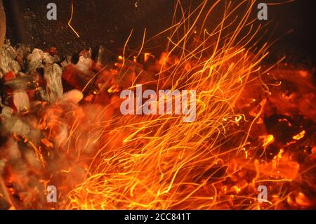 Sheaf of sparks fly from bonfire. Bright trails of flame sparks. Burning traces glowing over black backdrop. Abstract fiery background Stock Photo