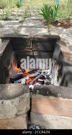 Rustic oven made from cracked burnt red bricks with smoky surface. Flaming fire inside old brazier. Bonfire flames in outdoor mangal Stock Photo