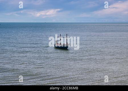 This unique photo shows a traditional Thai wooden fishing boat floating in the Pacific Ocean with calm seas and blue skies with white clouds. Stock Photo