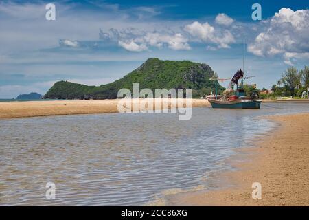 This unique photo shows a fishing boat running aground on the beach in Thailand and the Pak Nam Pran mountain range in the background Stock Photo