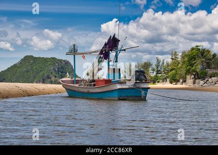 This unique photo shows a fishing boat running aground on the beach in Thailand and the Pak Nam Pran mountain range in the background Stock Photo