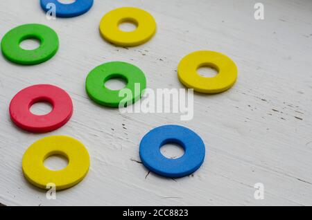 Multi-colored details of the children's constructor on a wooden background. Random round fragments are chaotic. Selective focus. Stock Photo