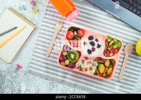 Lunch box with vegetable salad, berries in yougurt, fruits and rice on office table Stock Photo