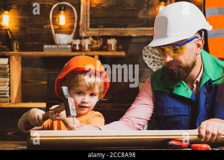 Cute little son and father in hard hat holding wooden plank and hammer. Boy helping his dad at home. Stock Photo