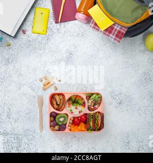 Open lunch box with healthy food near backpack and laptop on grey background with copy space Stock Photo