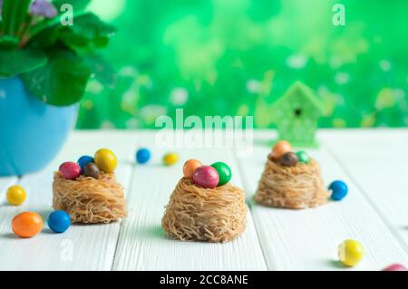 Painted chocolate eggs in sweet nests over white wooden background Stock Photo
