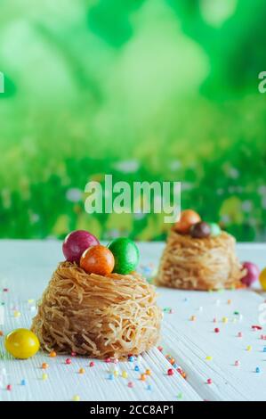 Painted chocolate eggs in sweet nests on white wooden background Stock Photo
