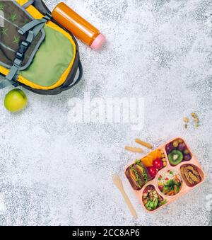 Open lunch box with sandwiches and fresh vegetables and fruits on the grey background Stock Photo