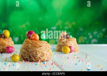Painted chocolate eggs in sweet nests over white wooden background Stock Photo