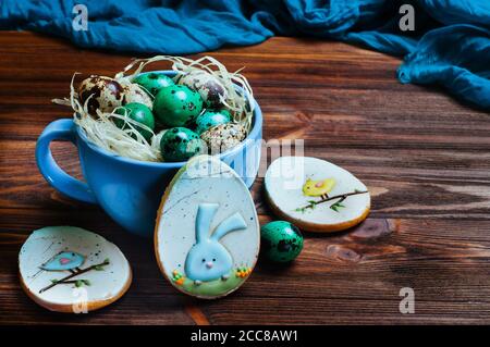 Painted quail eggs in a cup and Easter egg-shape gingerbreads on wooden table Stock Photo