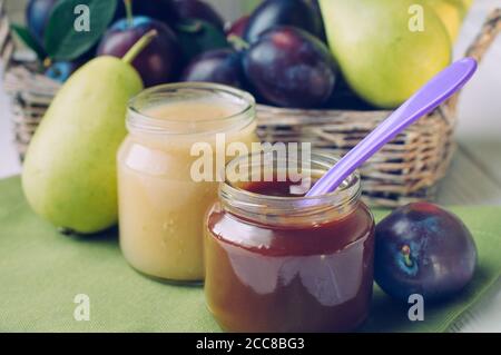 Two jars with prune and pear puree on the table near fresh fruits Stock Photo