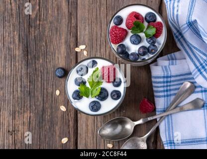 White yogurt in two bowls with blueberries and raspberries on natural wooden desk, flat view. Stock Photo
