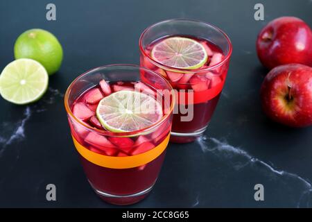 Two Glasses of Red Wine Sangria on the Table with Blurry Limes and Apples in the Background Stock Photo
