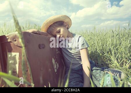 Young cowboy relaxes over his heavy suitcase in a meadow Stock Photo