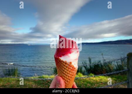 Red and white ice cream cone held up to the hot summer sky in front of a lake Taupo. New Zealand Stock Photo