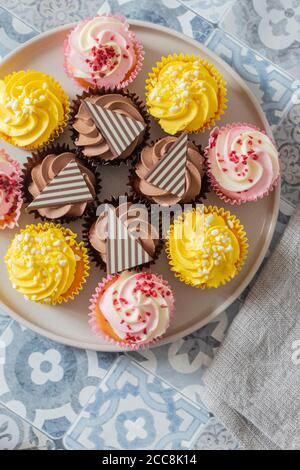 Variety of cupcakes on a grey plate.  Blue patterned tile background Stock Photo