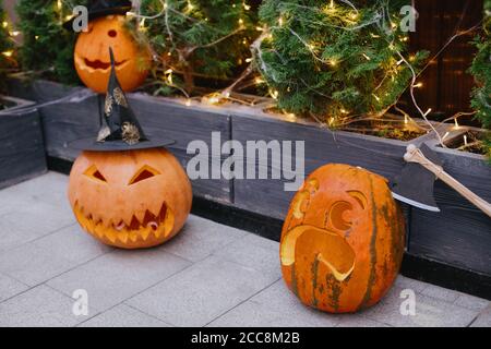 Halloween street decor. Carved pumpkins with scary face, witch hat  and ax, modern festive decoration of european street. Happy Halloween Stock Photo