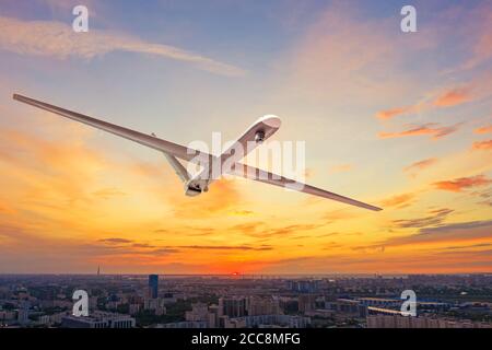 Unmanned military drone uav flying in the air over the city in evening sunset Stock Photo