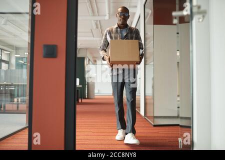 African young man carrying box with things while walking along the office corridor he getting a new job