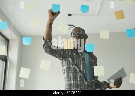 African businessman in casual clothing writing new ideas on adhesive notes on glass wall he working at office Stock Photo