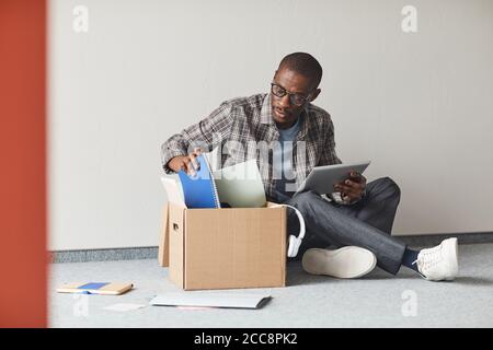 African young man sitting on the floor unpacking the box with documents and using digital tablet Stock Photo