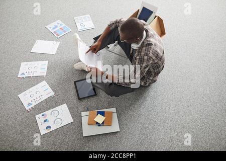 High angle view of African businessman sitting on the floor and examining business charts and graphs Stock Photo