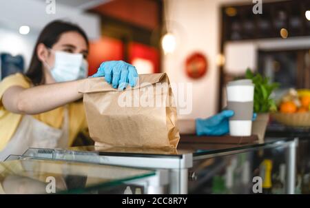 Bar owner working only with take away orders during corona virus outbreak - Young woman worker wearing face surgical mask giving takeout meal Stock Photo
