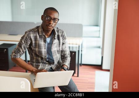 Portrait of African designer in eyeglasses looking at camera while using his laptop computer at work Stock Photo