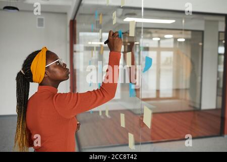 African woman making notes on adhesive notes on the glass wall she planning her working day Stock Photo