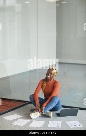 African businesswoman sitting on the floor with laptop and business documents and working in empty modern office Stock Photo