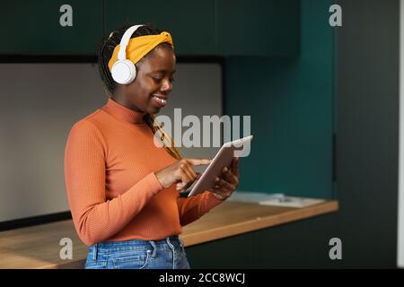 African happy designer wearing wireless headphones typing on digital tablet she working online at office Stock Photo