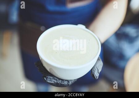 Barista wearing medical latex black gloves, making cappuccino, bartender preparing coffee drink. Blurred image, selective focus Stock Photo