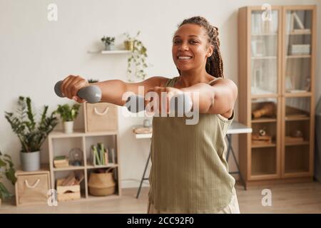 Young smiling woman standing and exercising dumbbells in the room at home Stock Photo